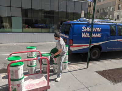 A staff member carrying a green container and a blue commercial van parked on the side of the road.