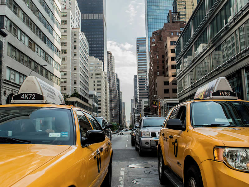 A city with many white and brown buildings, yellow taxis on the road, cars, and a clear sky.